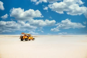 Yellow truck riding on the sandy ground under the cloudy blue sky