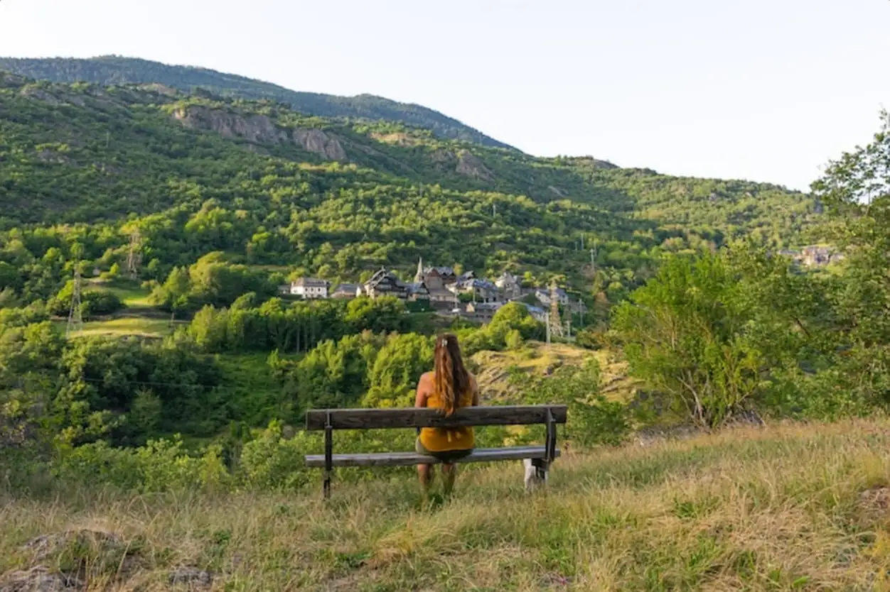 Beautiful shot of a woman sitting on the bench facing a mountain landscape