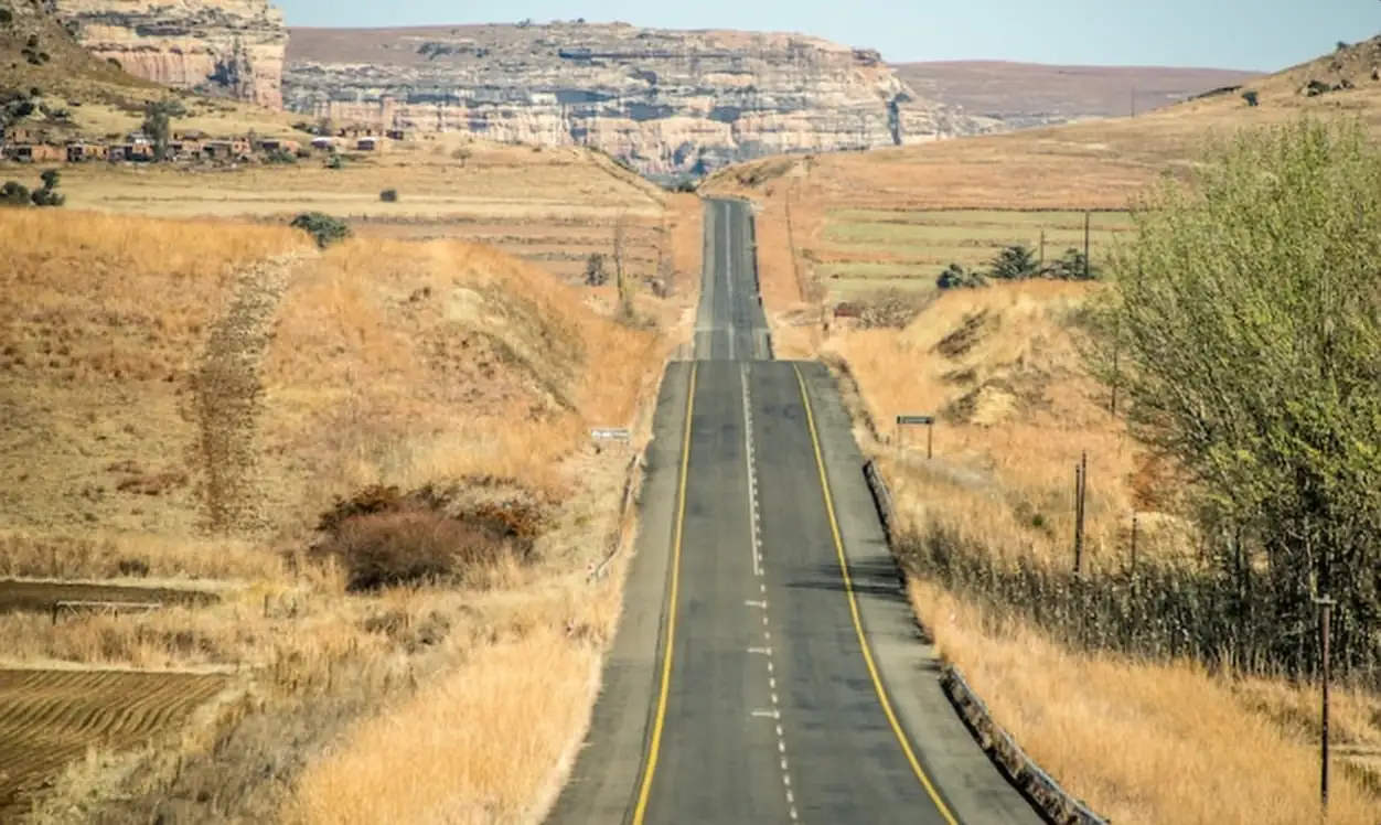 Wide angle shot of a road going on a mountain surrounded by bushes and dry grass